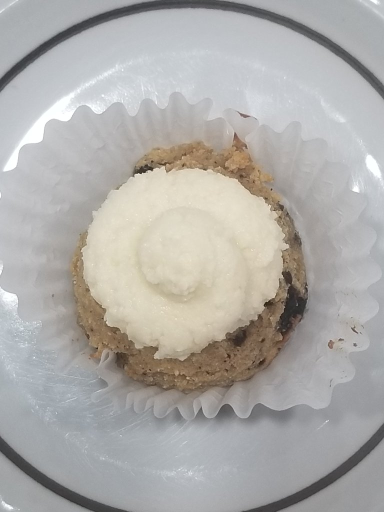 A cupcake with a swirl of white frosting on top inside a paper liner on a small plate.