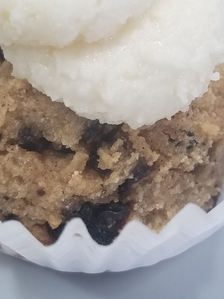 This is a close up of a cupcake where you can see the red fruit.  There is white frosting on top and the cake is inside a white paper wrapper.